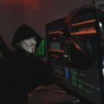Haker w masce Guy Fawkesa przy komputerze w ciemnym pokoju