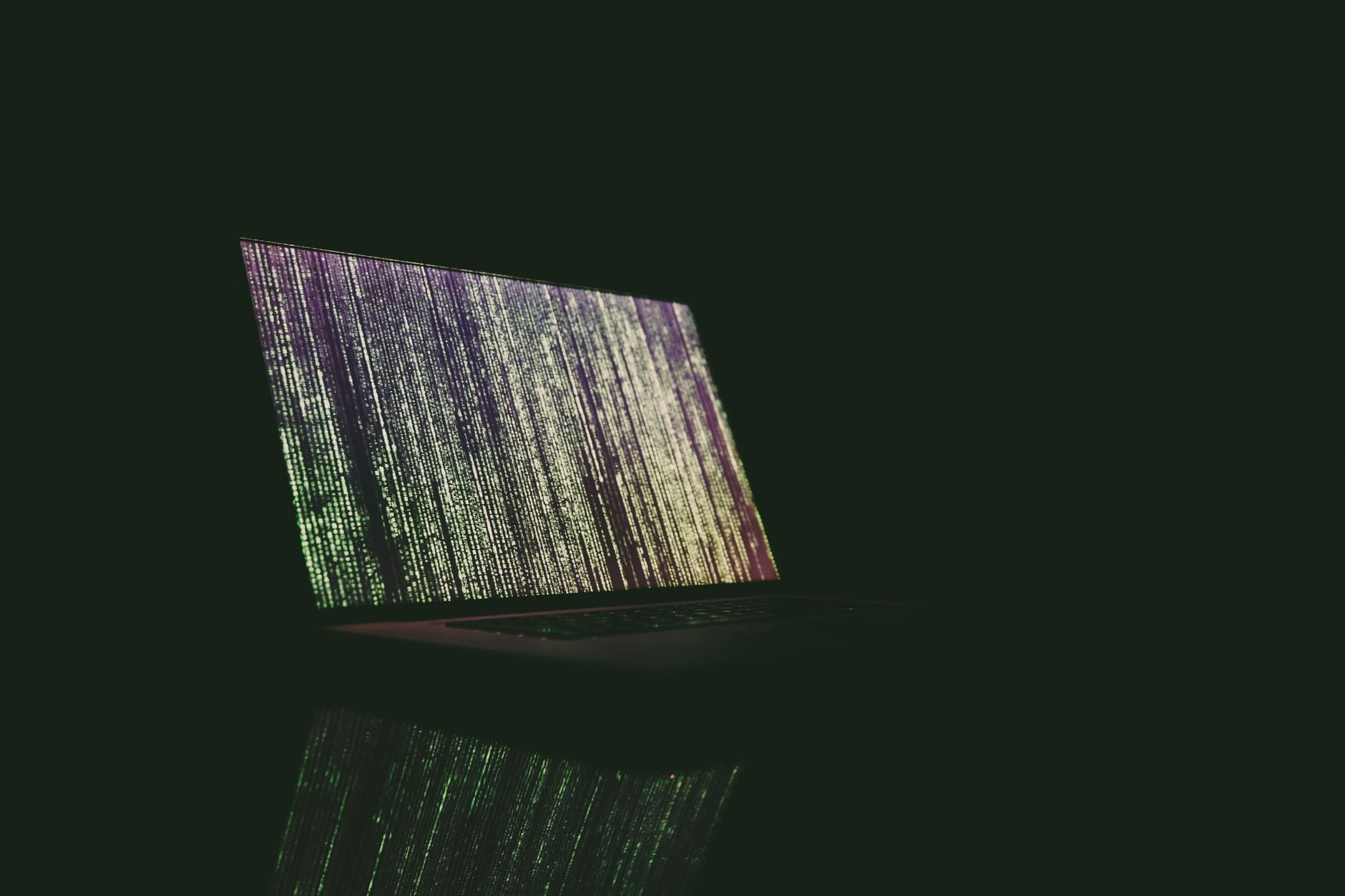 Laptop z zielonym i fioletowym kodem na ekranie w ciemnym pokoju