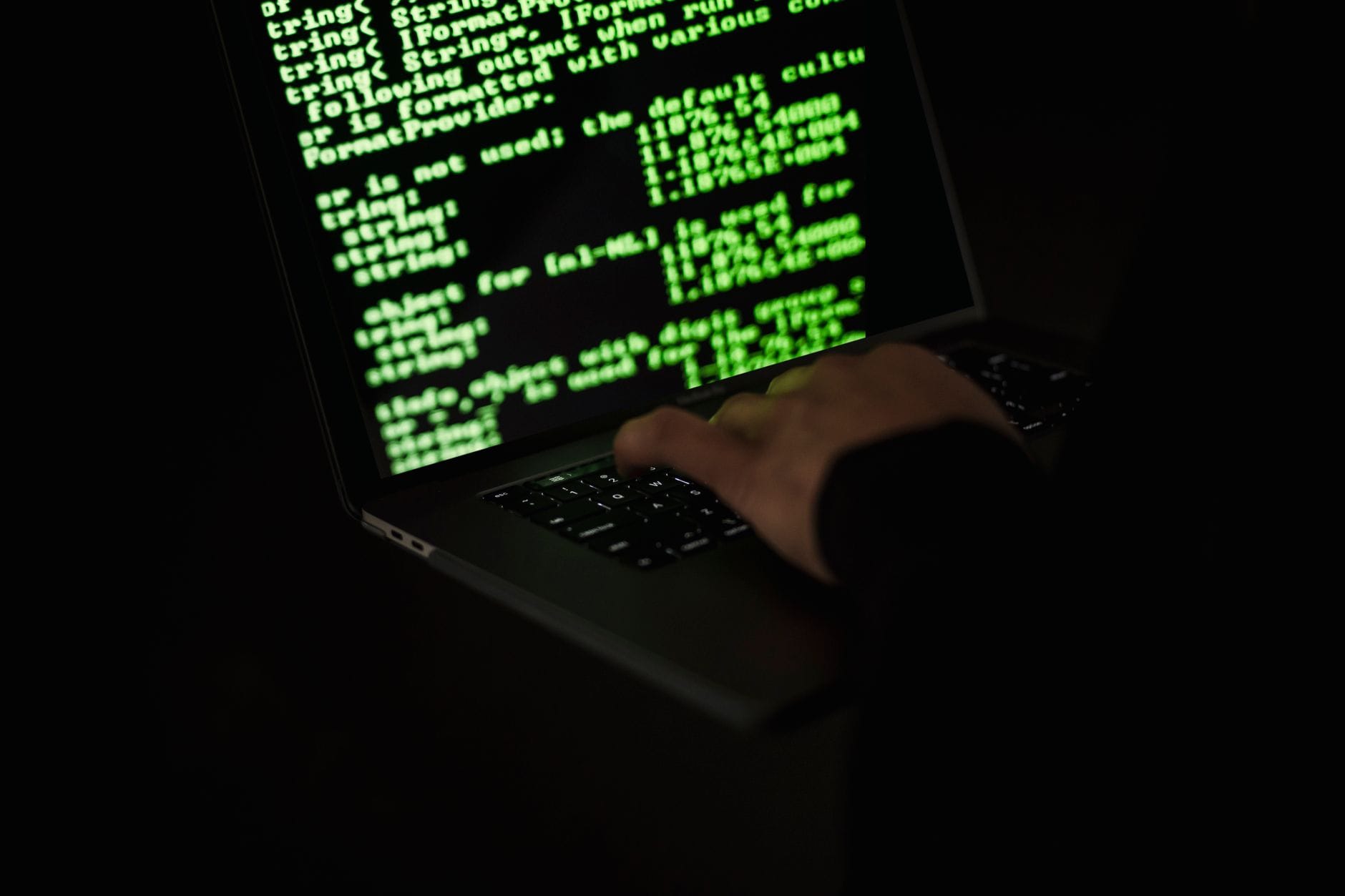 VPN płatny czy darmowy: porównanie bezpieczeństwa i wydajności Osoba pisząca kod na netbooku w ciemności, motyw cyberbezpieczeństwa