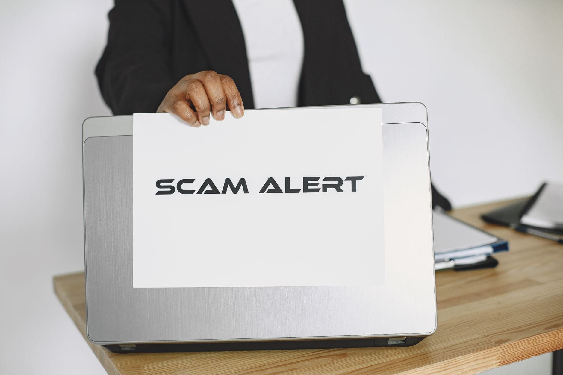 Osoba trzyma tabliczkę scam alert przy laptopie, ostrzegając przed oszustwem